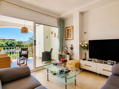 Lumineux salon avec sol effet marbre, s'ouvrant sur une terrasse privée aménagée de mobilier en osier et offrant des vues verdoyantes.