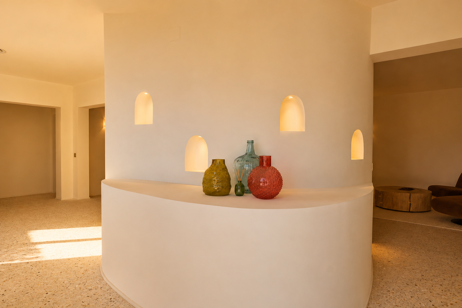 Mur de séparation incurvé avec quatre niches arquées éclairées et une étagère intégrée présentant des vases décoratifs, sur un sol en terrazzo.