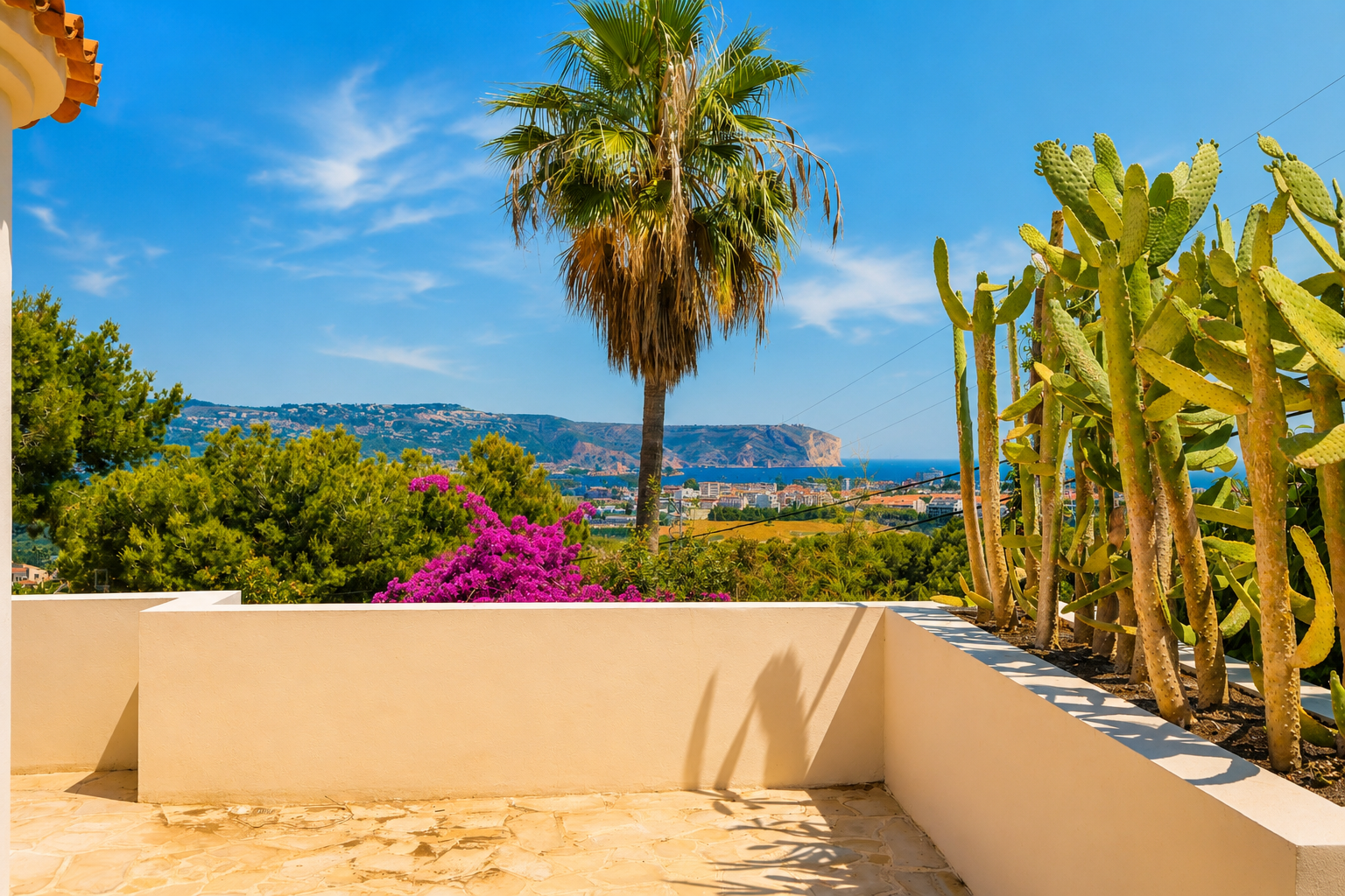 Terrasse avec un sol en pierre irrégulière et un muret beige. Elle présente un jardin de cactus et des vues panoramiques sur la mer Méditerranée, la côte et un cap lointain.