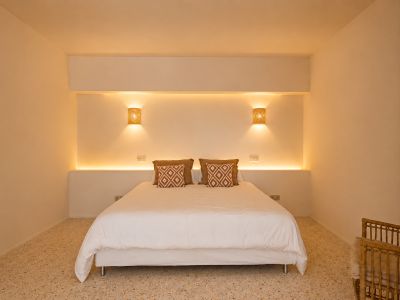 Chambre avec lit double, éclairage LED intégré dans la tête de lit et appliques murales en osier. Sol en terrazzo et coussins décoratifs.