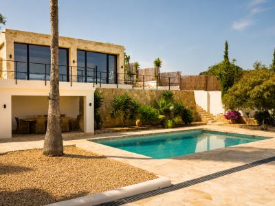 L'extérieur en terrasses de la villa révèle une piscine rectangulaire sur pavés de pierre irréguliers, un coin repas extérieur couvert et une façade en pierre avec grandes fenêtres.