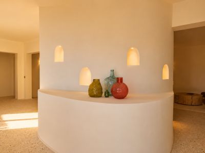 Mur de séparation incurvé avec quatre niches arquées éclairées et une étagère intégrée présentant des vases décoratifs, sur un sol en terrazzo.