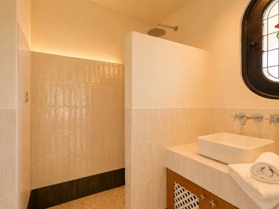 Salle de bain moderne avec douche à l'italienne, pommeau de pluie et éclairage LED indirect. Lavabo vasque sur meuble carrelé et fenêtre ovale en vitrail ornée d'une rose.