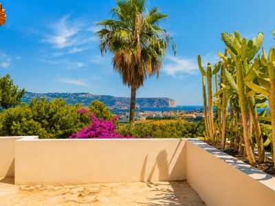 Terrasse avec un sol en pierre irrégulière et un muret beige. Elle présente un jardin de cactus et des vues panoramiques sur la mer Méditerranée, la côte et un cap lointain.