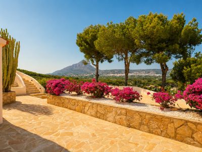 Terrasse extérieure avec pavé en pierre naturelle, escalier courbé et bougainvilliers éclatants. Un grand cactus et des vues panoramiques sur les montagnes et la ville.