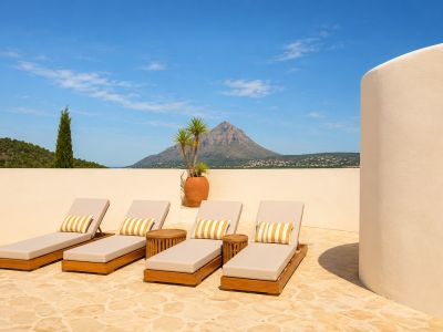 Terrasse solarium avec quatre chaises longues en bois, coussins rayés, pavé en pierre et vues panoramiques sur le Montgó et la mer lointaine.