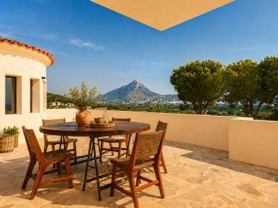 Vaste terrasse extérieure avec sol en dalles irrégulières et mobilier de repas en bois rustique. Vue panoramique sur le Montgó et la vallée sous un ciel clair.
