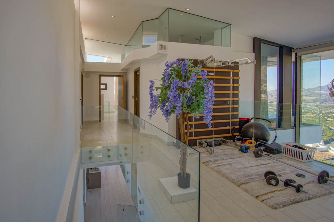 Espace de gym à l'étage supérieur avec des balustrades en verre modernes et un sol clair. Équipé d'une espalier et de poids, il offre des vues panoramiques par de grandes baies vitrées.