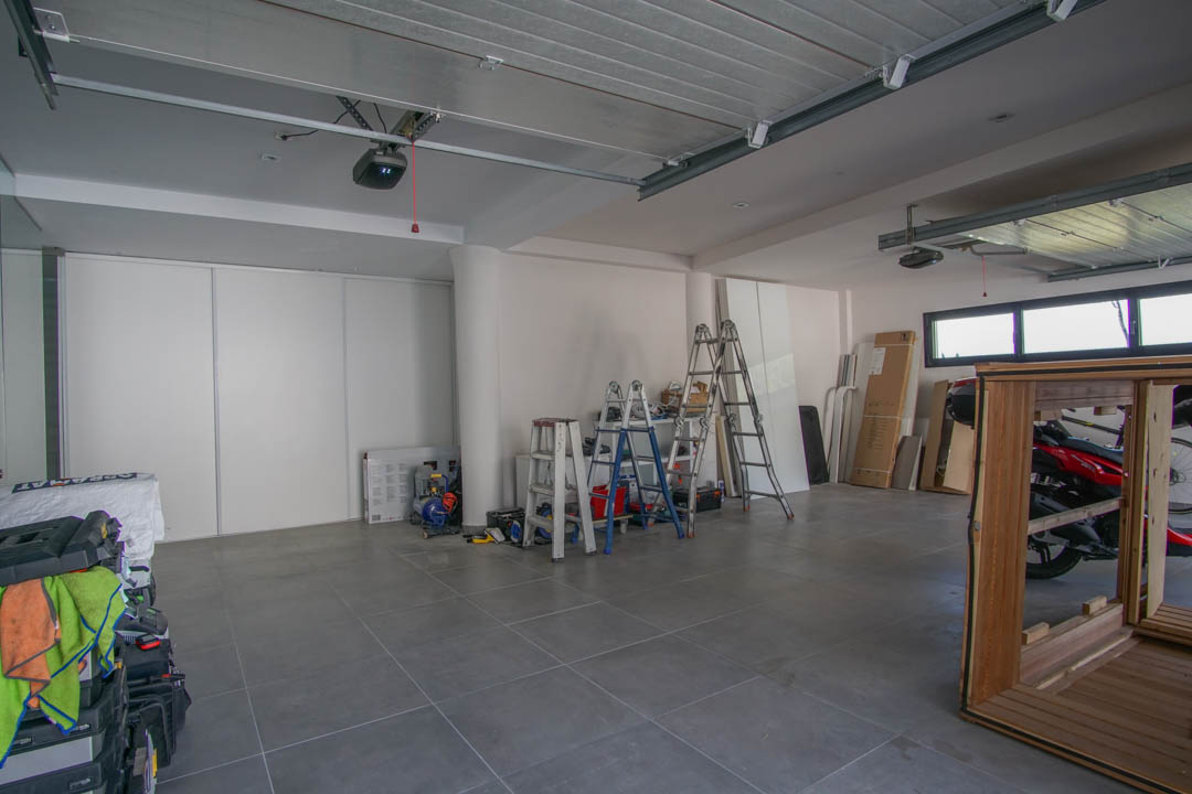 Grand garage avec sol carrelé gris et murs blancs. Il dispose de deux mécanismes de porte automatique, de fenêtres horizontales et de portes coulissantes pour le rangement.