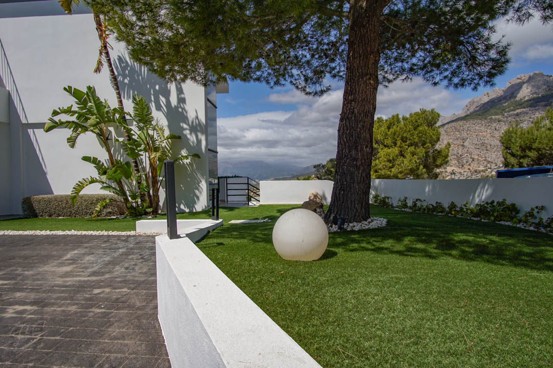 L'extérieur de la villa comprend une entrée pavée, une pelouse artificielle avec un pin mature, un luminaire sphérique moderne et des vues sur la montagne.