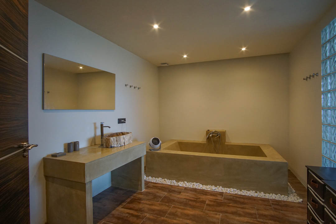 Salle de bain moderne avec une vasque en bois rustique sur un meuble effet béton, une baignoire intégrée et un mur en pavés de verre.