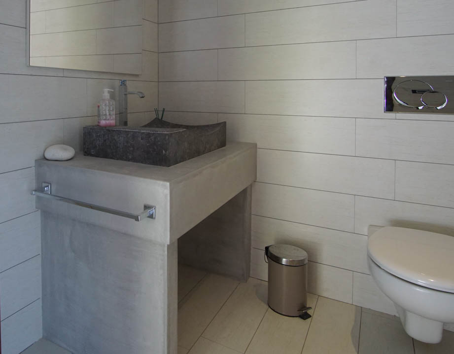 Toilettes d'invités modernes avec lavabo en pierre sur meuble-vasque effet béton et carrelage clair. WC suspendu avec plaque de chasse chromée.