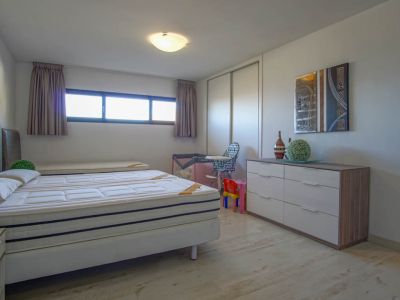 Chambre lumineuse dotée d'un lit avec deux matelas, d'un sol imitation bois clair et d'une longue fenêtre horizontale. Elle comprend une armoire coulissante blanche et une commode moderne surmontée d'une œuvre abstraite.