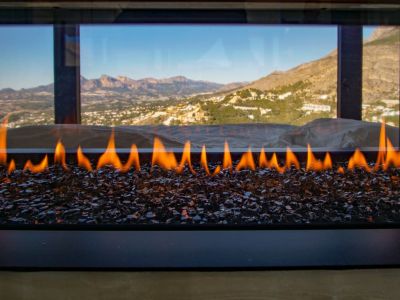 Cheminée à gaz contemporaine avec flammes sur lit de verre sombre, offrant une vue panoramique sur les montagnes et la vallée.