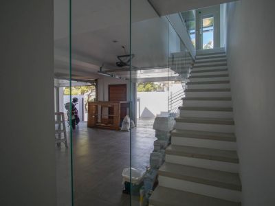 Escalier intérieur moderne avec balustrade en verre et marches claires, jouxtant un garage carrelé avec porte ouverte et lumière naturelle.