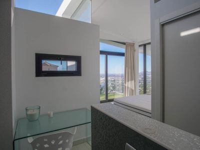 Espace bureau avec un pupitre en verre et fenêtre horizontale, offrant des vues panoramiques sur la mer et la ville depuis la chambre adjacente.