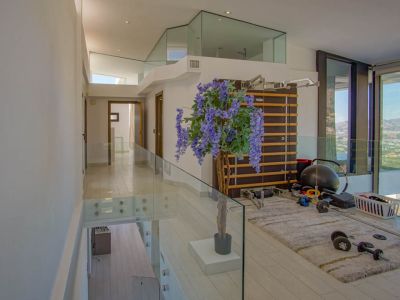 Espace de gym à l'étage supérieur avec des balustrades en verre modernes et un sol clair. Équipé d'une espalier et de poids, il offre des vues panoramiques par de grandes baies vitrées.