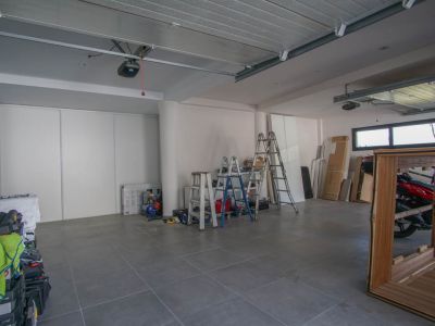 Grand garage avec sol carrelé gris et murs blancs. Il dispose de deux mécanismes de porte automatique, de fenêtres horizontales et de portes coulissantes pour le rangement.