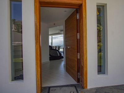 L'entrée principale ouverte révèle une porte et un cadre en bois à panneaux, flanqués de fenêtres verticales, offrant un aperçu de l'intérieur moderne et des vues sur la montagne.