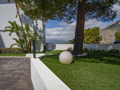 L'extérieur de la villa comprend une entrée pavée, une pelouse artificielle avec un pin mature, un luminaire sphérique moderne et des vues sur la montagne.