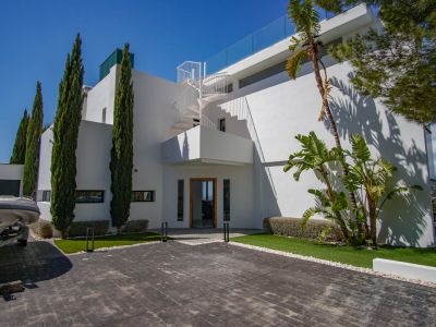 L'extérieur de la villa moderne présente une allée pavée, des cyprès élancés et un escalier en colimaçon blanc menant à la terrasse supérieure avec balustrade en verre.