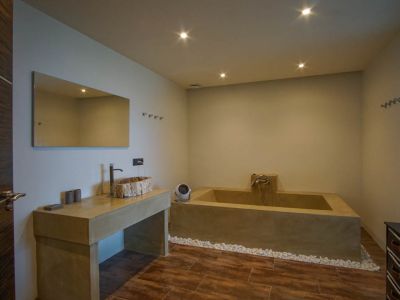 Salle de bain moderne avec une vasque en bois rustique sur un meuble effet béton, une baignoire intégrée et un mur en pavés de verre.