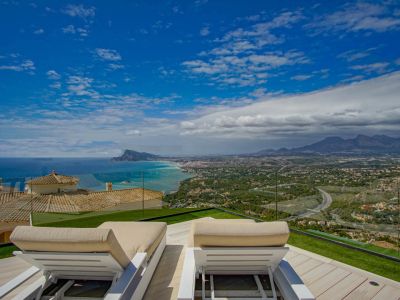 Terrasse sur le toit avec deux chaises longues blanches sur une terrasse en bois clair et gazon artificiel, offrant une vue panoramique sur la mer Méditerranée, la côte d'Altea et les montagnes.