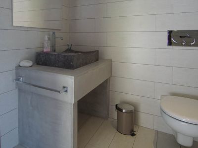 Toilettes d'invités modernes avec lavabo en pierre sur meuble-vasque effet béton et carrelage clair. WC suspendu avec plaque de chasse chromée.