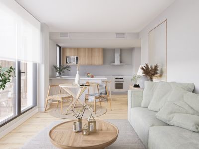 Espace de vie ouvert et lumineux avec canapé vert clair, table basse en bois et coin repas avec chaises tressées. La cuisine moderne intègre des armoires en bois clair et des appareils, baignée de lumière naturelle.