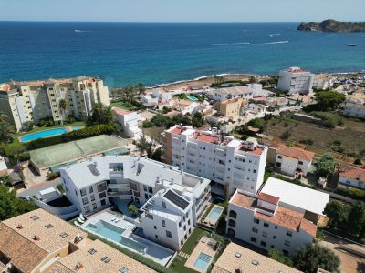 Vue aérienne de la côte de Jávea, révélant des complexes résidentiels avec piscines et un court de tennis, face à la Méditerranée et un cap lointain.