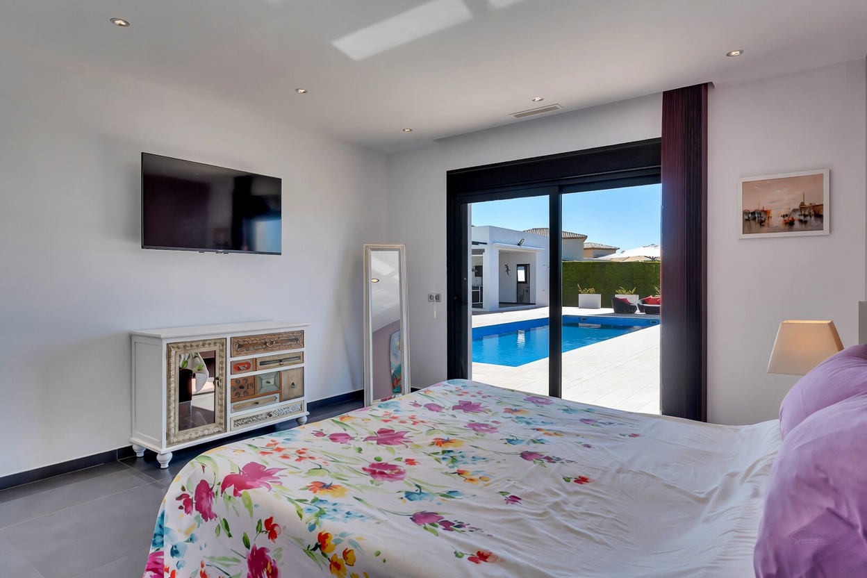 Chambre lumineuse avec accès direct à la piscine et à la terrasse via des baies vitrées, dotée d'une literie fleurie, d'une TV murale et d'une commode décorative.