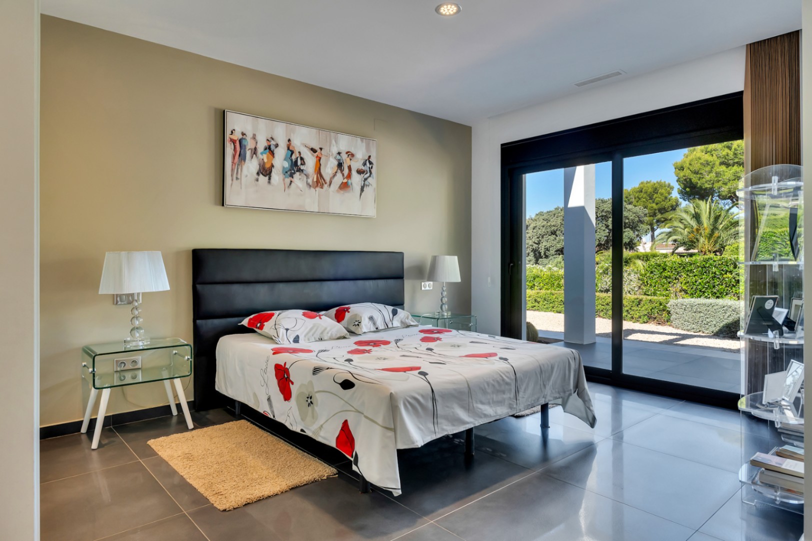 Chambre lumineuse avec accès direct au jardin par de grandes portes coulissantes, carrelage foncé et tables de chevet en verre.