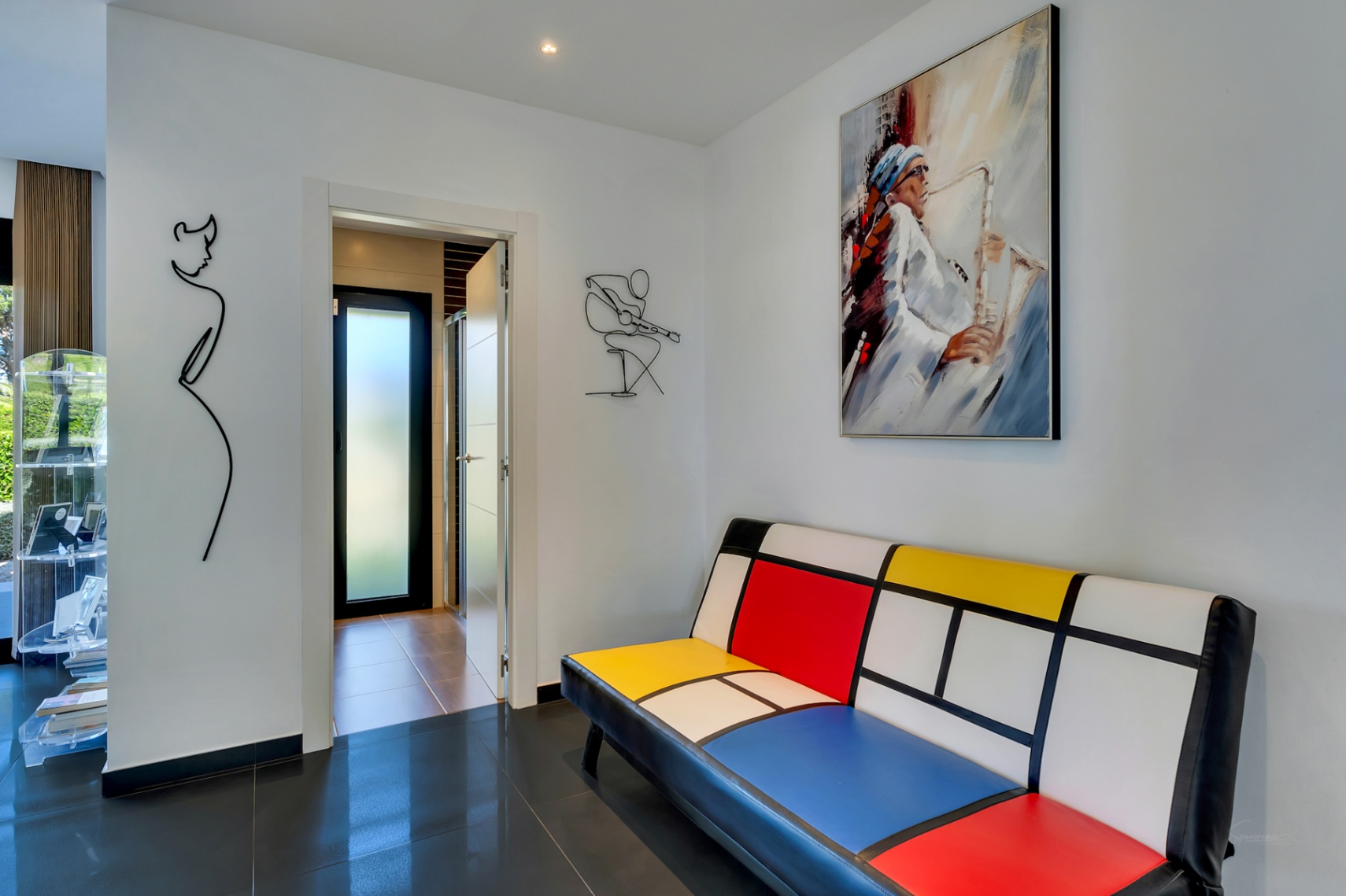 Couloir moderne avec un canapé style Mondrian, une peinture de saxophoniste et des œuvres d'art murales en fil de fer, sur carrelage sombre brillant.