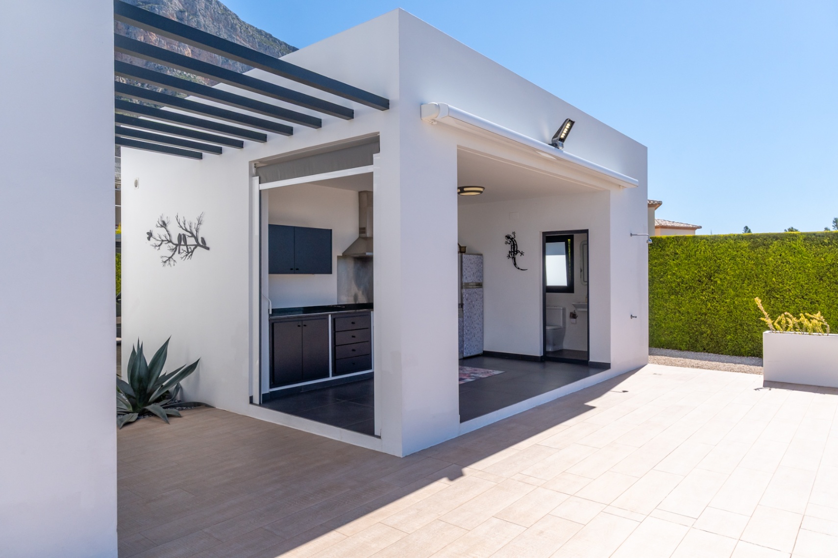 Cuisine extérieure moderne et espace barbecue avec des meubles sombres, intégrant une salle de bain extérieure pratique, sur une terrasse carrelée avec vue sur la montagne.
