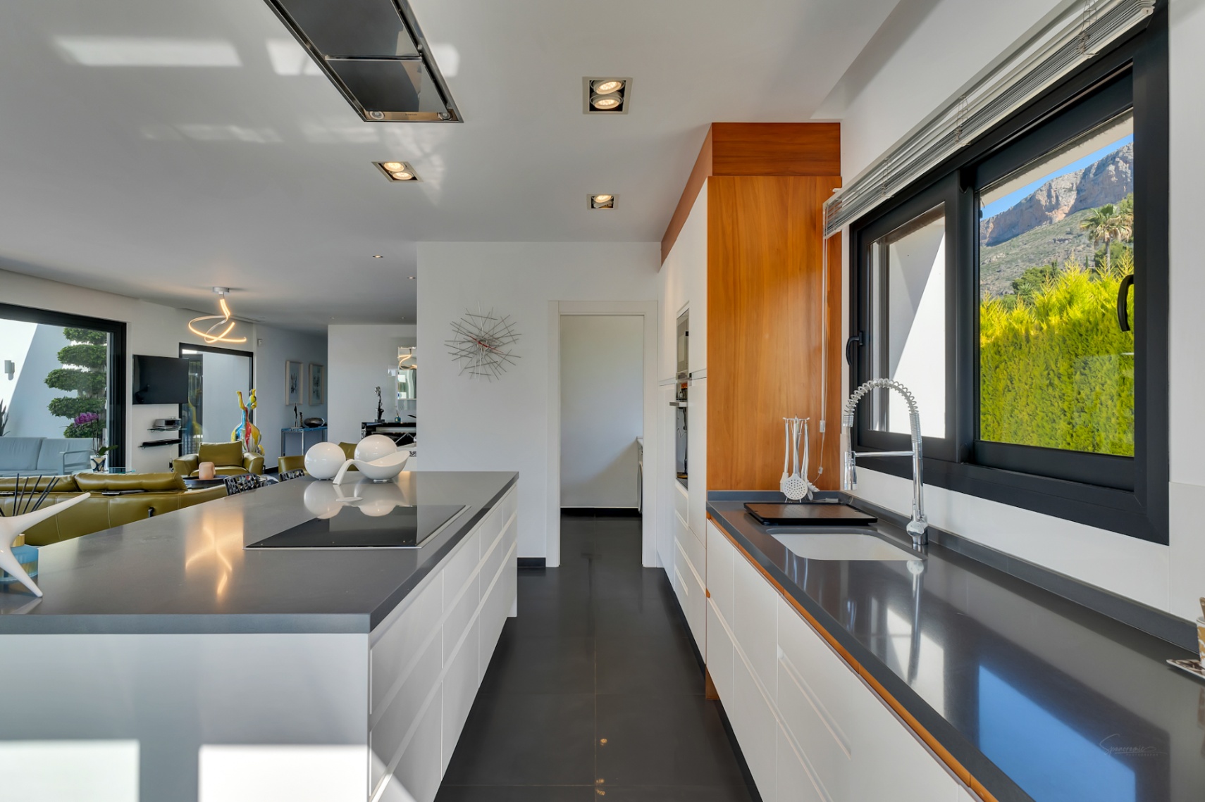 Cuisine ouverte moderne avec plans de travail en quartz gris, armoires blanches sans poignées, plaque à induction intégrée sur l'îlot et vue sur la montagne depuis la fenêtre.