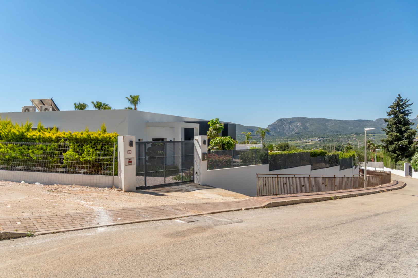 Extérieur de la villa moderne avec portail d'entrée, haies vertes et vues lointaines sur le Montgó depuis la rue.