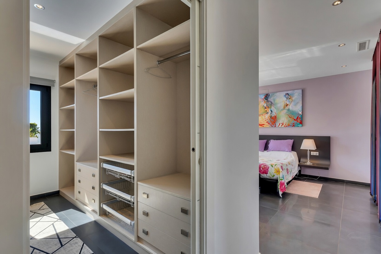 Grand dressing avec étagères intégrées, tiroirs et paniers coulissants, attenant à une chambre aux murs lavande et œuvre d'art murale.