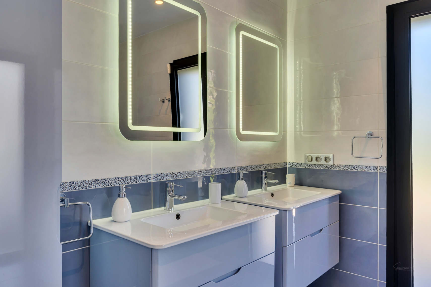 Salle de bain contemporaine avec double vasque suspendue bleu clair, plans de travail blancs et deux miroirs LED au-dessus de murs carrelés bleus et gris.