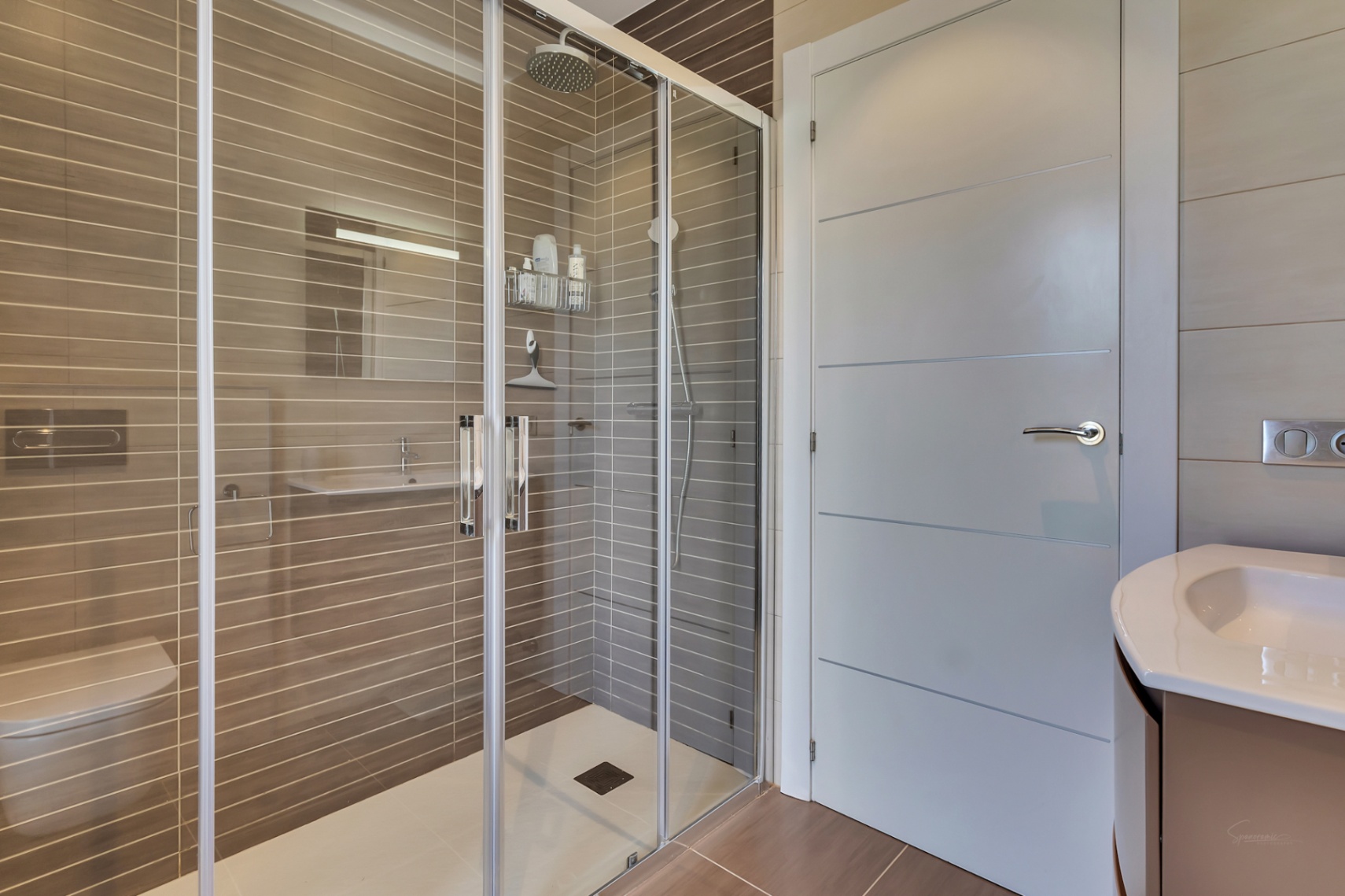 Salle de bain moderne avec douche à l'italienne spacieuse, paroi vitrée, pommeau de pluie et carrelage taupe à rayures horizontales. Comprend des toilettes suspendues et un meuble-lavabo.