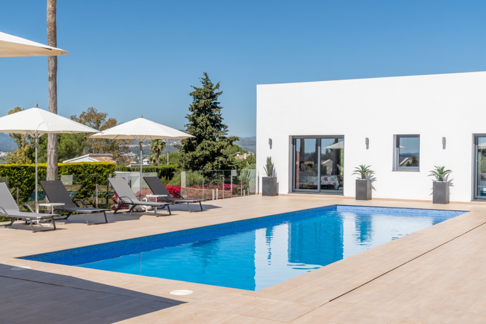 Vaste terrasse avec mobilier d'extérieur clair, piscine bleue invitante et vue sur la végétation luxuriante, propice à la détente.