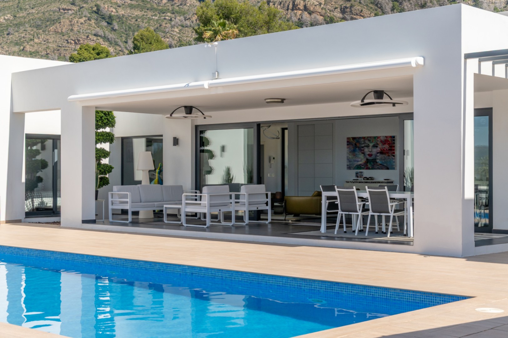 Vaste terrasse couverte avec store rétractable, salon et salle à manger extérieurs, attenante à la piscine et à l'intérieur, vue montagne.
