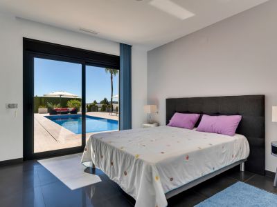 Chambre avec carrelage foncé et accès direct à la piscine extérieure, comprenant un espace détente avec canapé rouge et parasol sous un ciel bleu clair.