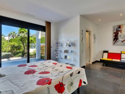 Chambre avec de grandes portes coulissantes vitrées s'ouvrant sur un jardin méditerranéen luxuriant, sol en carrelage foncé et mobilier moderne.