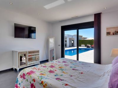 Chambre lumineuse avec accès direct à la piscine et à la terrasse via des baies vitrées, dotée d'une literie fleurie, d'une TV murale et d'une commode décorative.