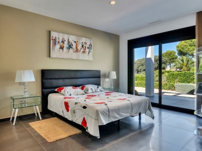 Chambre lumineuse avec accès direct au jardin par de grandes portes coulissantes, carrelage foncé et tables de chevet en verre.