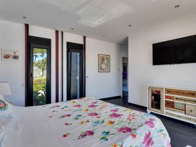 Chambre lumineuse avec lit à motifs floraux, accès direct au jardin par des portes vitrées et une commode unique à tiroirs variés.