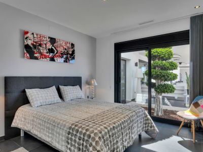 Chambre moderne avec lit double et tête de lit gris foncé, agrémentée d'art contemporain. Une grande porte vitrée coulissante donne sur un patio privé avec un arbre étagé.