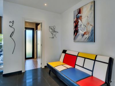 Couloir moderne avec un canapé style Mondrian, une peinture de saxophoniste et des œuvres d'art murales en fil de fer, sur carrelage sombre brillant.