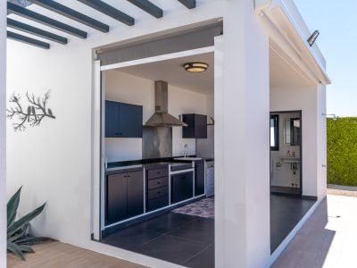 Cuisine extérieure avec armoires sombres et hotte en acier inoxydable, adjacente à une salle de bain extérieure pratique et une haie végétale.