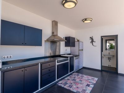 Cuisine extérieure avec des armoires bleu foncé, des comptoirs en pierre sombre, des appareils en acier inoxydable et une salle de bain indépendante attenante.